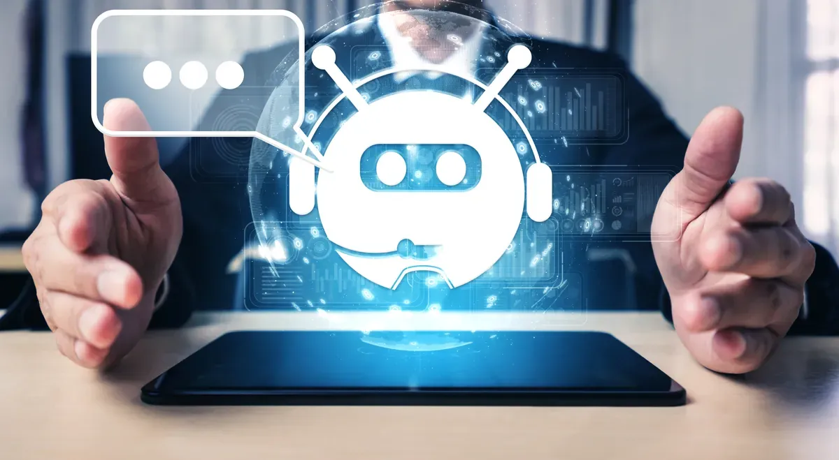 Tablet ekranının üzerinde yükselen yapay zekâ sohbet robotu simgesi ve onu iki yandan çevreleyen eller