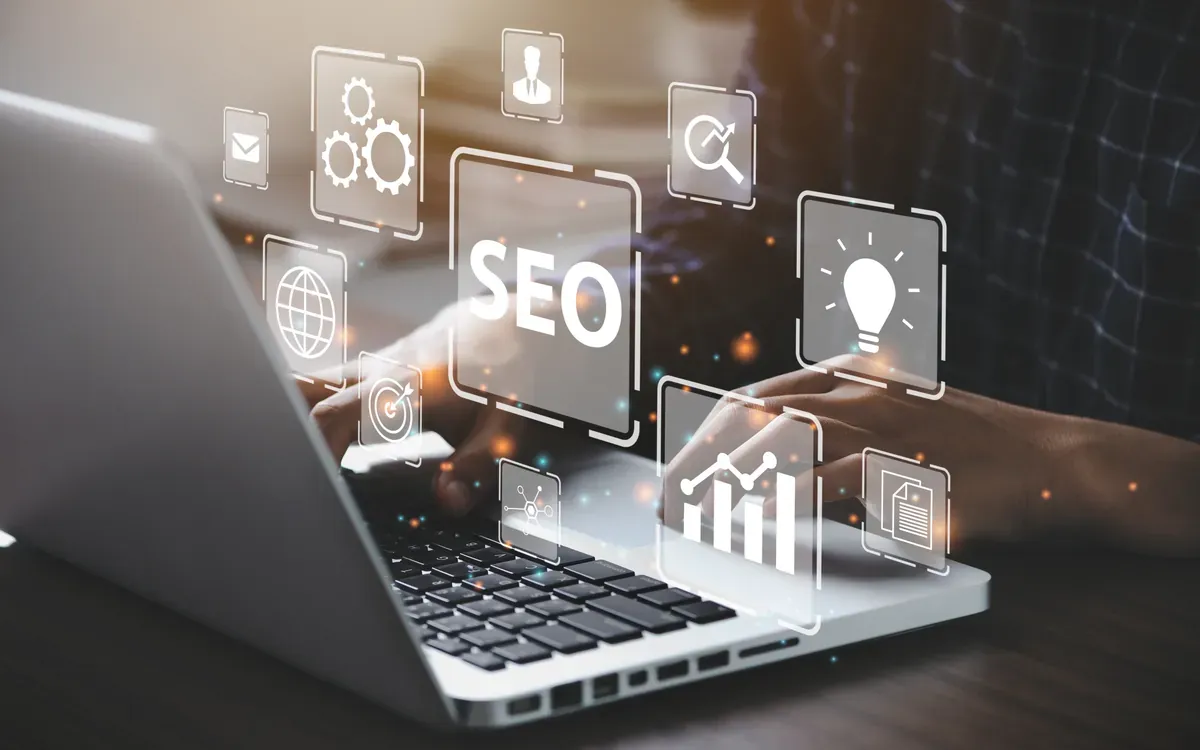Dizüstü bilgisayarda çalışan bir kişinin ekranı üzerinde beliren SEO, arama, fikir ve büyüme grafiği simgeleri