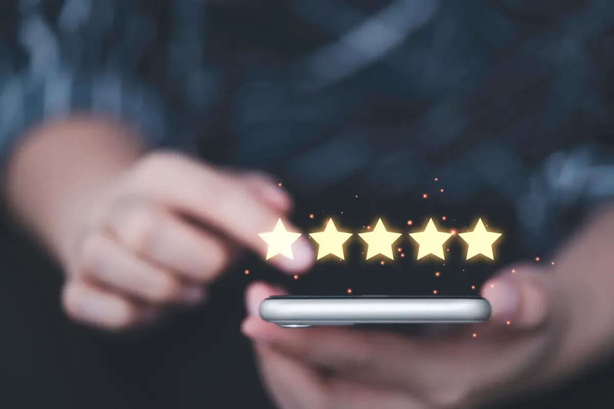 Akıllı telefon tutan bir elin üzerinde parlayan sarı beş yıldızlı müşteri değerlendirmesi simgesi, koyu arka plan