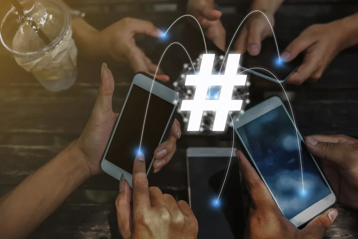 Masada bir araya gelmiş arkadaşların ellerindeki akıllı telefonların üzerinde beliren parlak hashtag simgesi