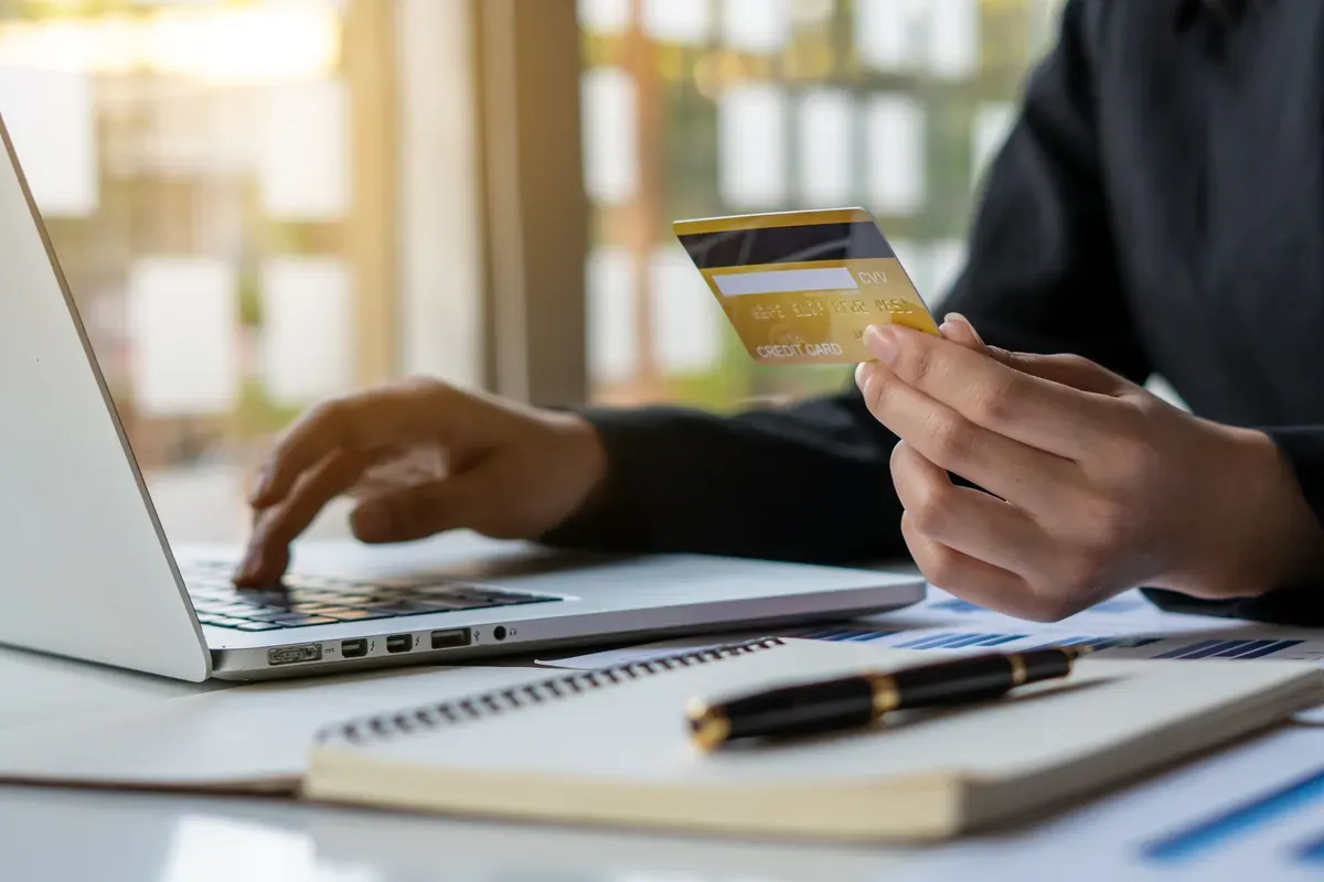Dizüstü bilgisayar başında kredi kartı bilgilerini girerek online ödeme yapan bir kişinin elleri