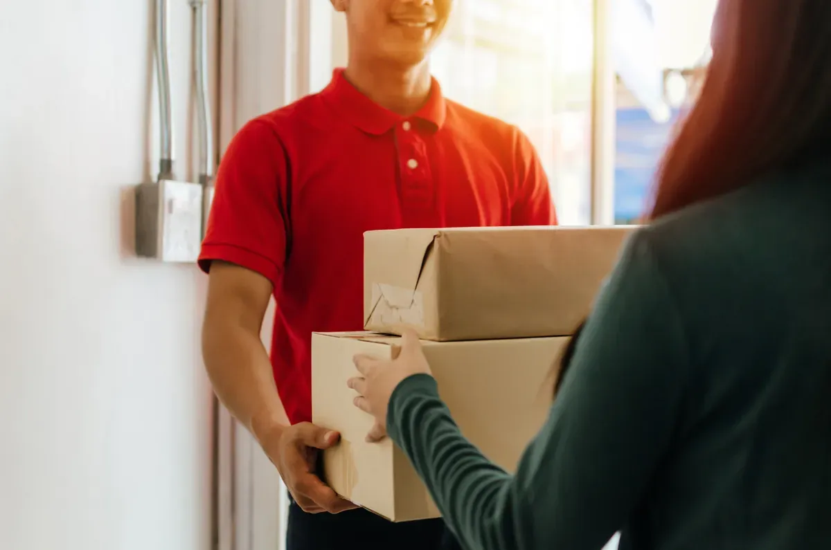 Kırmızı üniformalı kuryeden kapıda kargo paketlerini teslim alan bir müşteri