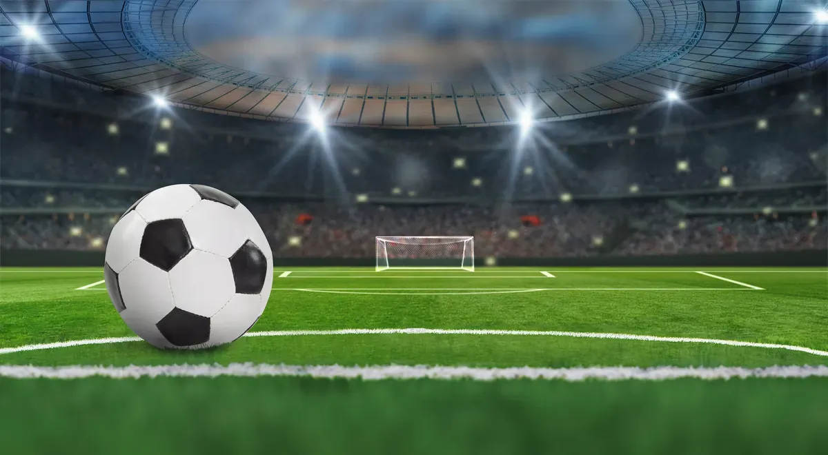 Işıklandırılmış bir futbol stadyumunda yeşil sahanın orta çizgisinde duran futbol topu