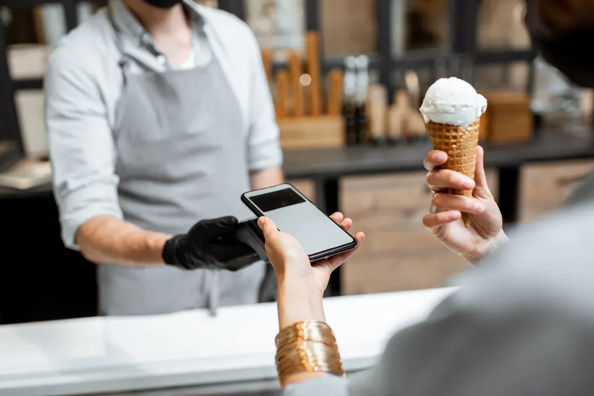 Küçük bir dükkânda müşterinin telefonla yaptığı temassız ödemeyi cihazıyla alan satıcı
