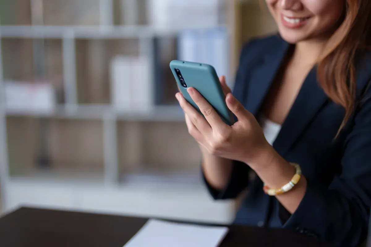 Ofiste akıllı telefonundan müşteri mesajlarına gülümseyerek yanıt veren bir iş kadını
