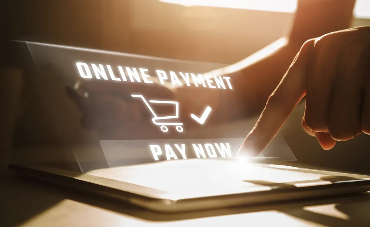 Tablet ekranının üzerinde beliren online ödeme ve alışveriş arabası simgesine parmağıyla dokunan bir kişinin eli